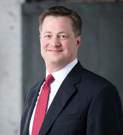 Middle-aged white male attorney in dark suit and red tie.
