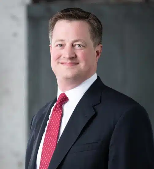 Middle-aged white male attorney in dark suit and red tie.