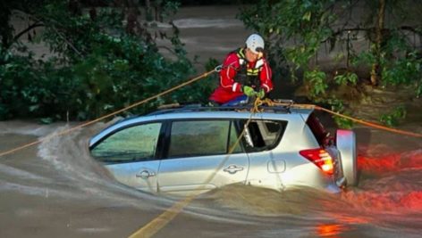 A motorist is helped by a first responder in a water rescue from flood waters along Valley Creek.