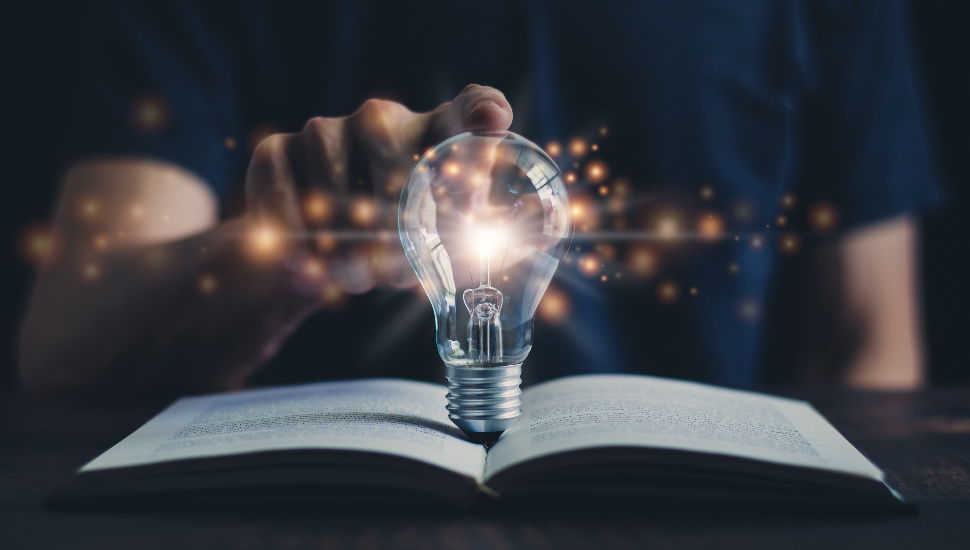 finger on a lightbulb on a book
