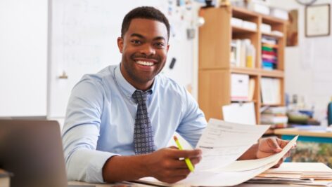 A Black man in a shirt and tie sitting at his desk looking at some papers