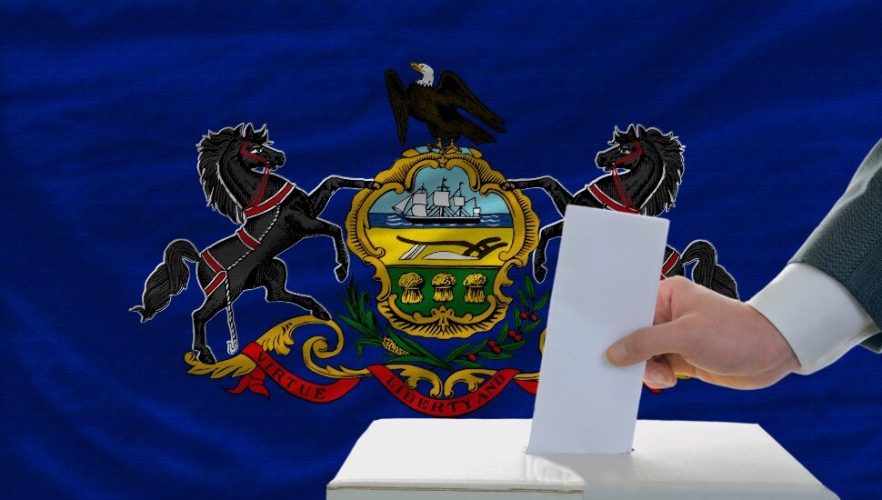 man putting ballot in a box during elections in front of flag american state of pennsylvania