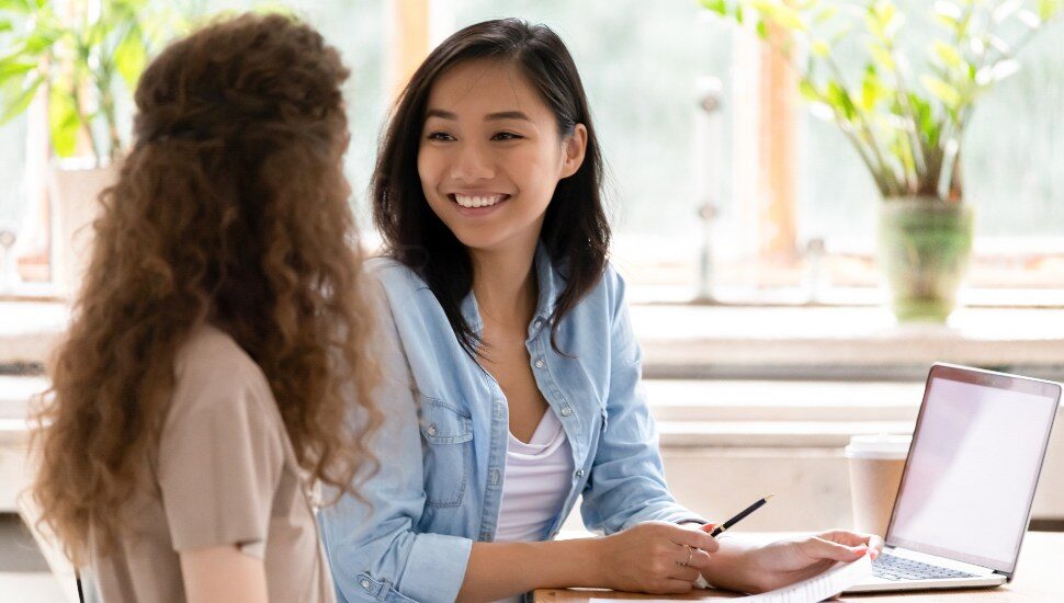 Smiling hr advisor meeting applicant at job interview consulting client about contract offer giving advice, happy diverse girls colleagues interns students discussing paperwork together