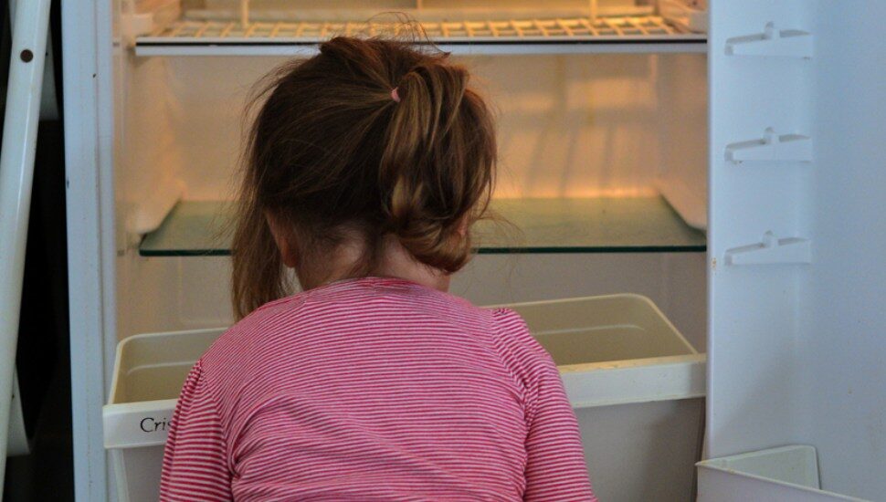little girl sitting at empty refrigerator
