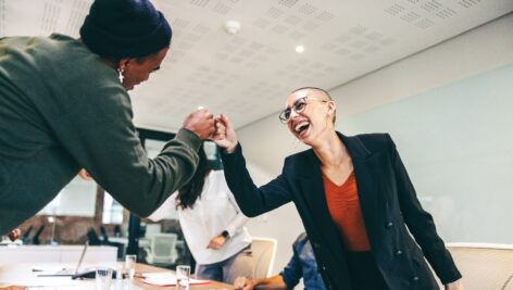 Young businesspeople fist bumping each other before a meeting in a boardroom. Two colleagues smiling cheerfully while greeting each other. Group of businesspeople attending a briefing in a modern office.
