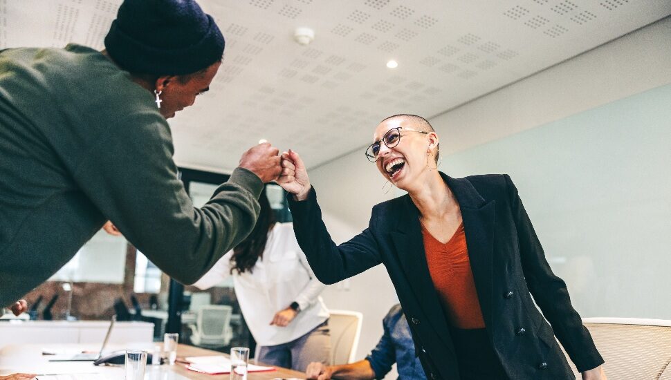 Young businesspeople fist bumping each other before a meeting in a boardroom. Two colleagues smiling cheerfully while greeting each other. Group of businesspeople attending a briefing in a modern office.