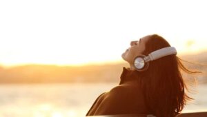 A woman with headphones by the water at sunset
