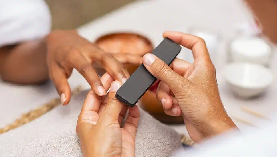 Close up of african hands of a qualified manicurist filing the nails of a young woman. Hands during manicure care session. Detail of a girl in a nail salon receiving manicure.