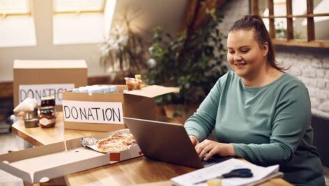 Young happy woman using laptop while collecting donations for charitable foundation.