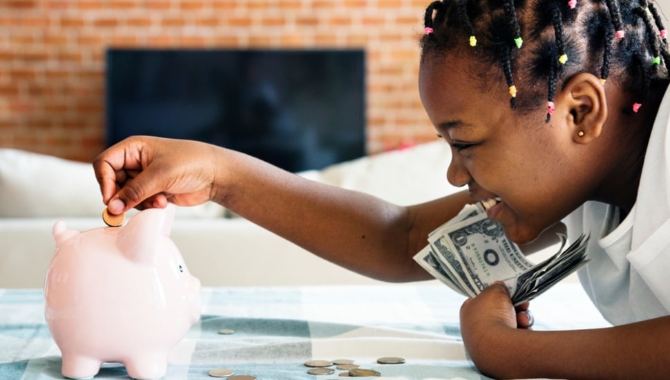 A little girl holding cash putting coins into a piggy bank