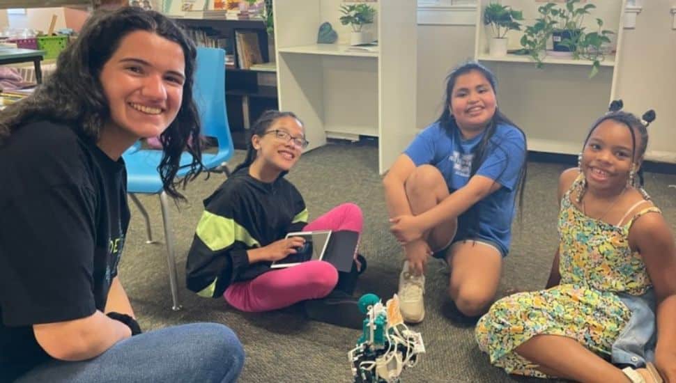 girls sitting in a circle around a small robot