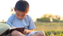 A child out in a field reading a book.