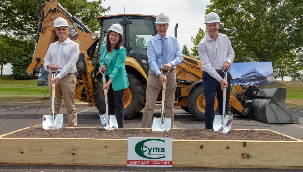 Almac Group groundbreaking, four people in construction hats breaking ground with shovel in front of excavator.