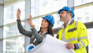 woman architect explaining blueprint to supervisor wearing safety vest at construction site.