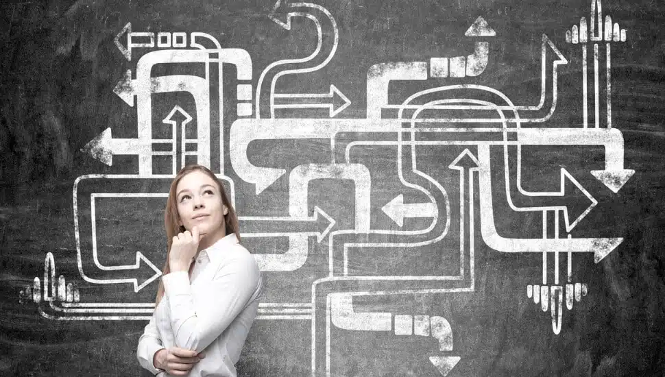 Woman standing in front a blackboard with arrows pointing in multiple directions.