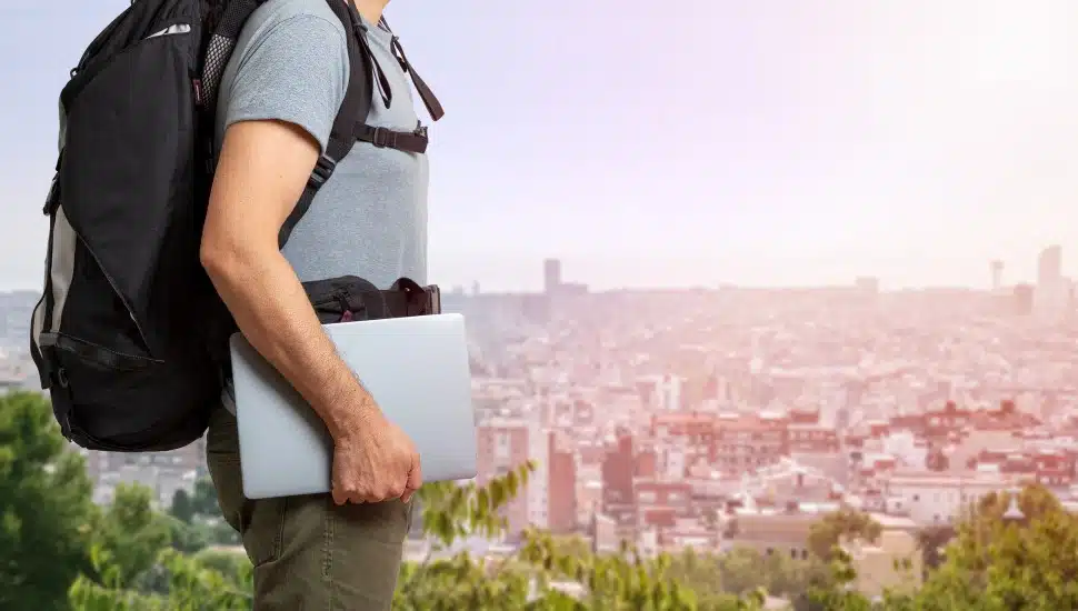 Unrecognizable digital nomad man traveling the world working with his laptop with a background city