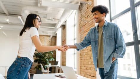 Cooperative young colleagues shaking hands at working desk in office