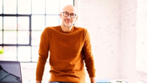 Portrait shot of smiling middle aged businessman wearing casual clothes while standing at office desk.