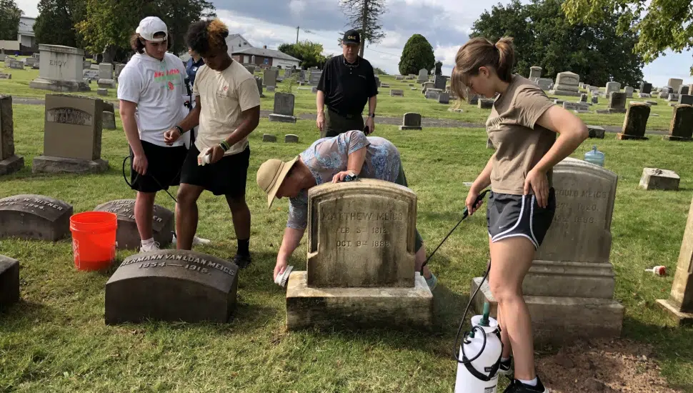 Hill Afternoon Community Service students learned how to effectively clean tombstones from Kelly Fenstermacher, pictured at work on the stone, who also has orchestrated the Walk to Remember historic Edgewood tour.
