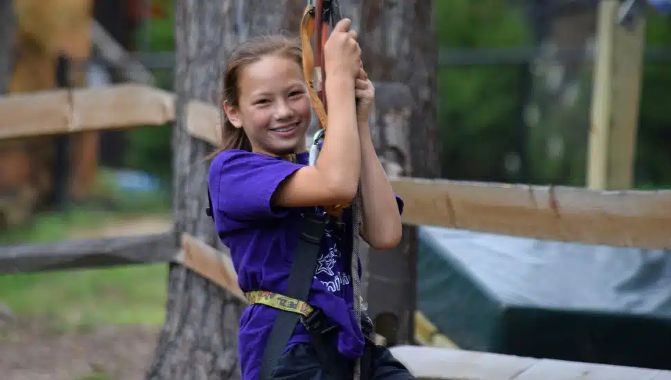 A young girl swinging through the Treetop Adventures at Elmwood Park Zoo.