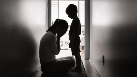 A child looks on as his seated mother weeps into her hands.