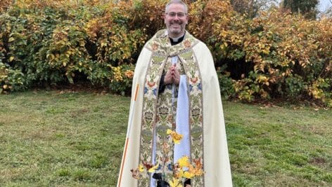 Father Tommy Thompson, rector of Washington Memorial Chapel, posing with the sapling from George Washington's beloved tulip poplar.