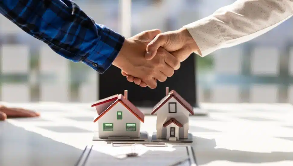 Two people shaking hands over house models.