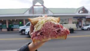A person holding up a sandwich outside of Hymie's Deli.