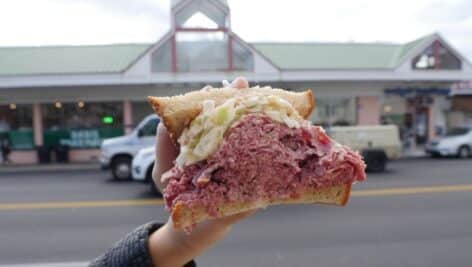 A person holding up a sandwich outside of Hymie's Deli.