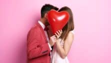 A couple kissing behind a heart balloon.
