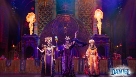 still image of three actors in costume on stage in front of flames