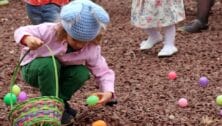 little girl with Easter basket picking up Easter egg.