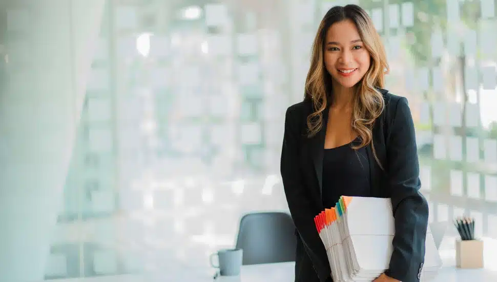 woman of East Asian decent standing in office holding fincancial documents
