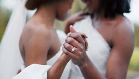 close-up shot of two African-American women holding hands in wedding dresses