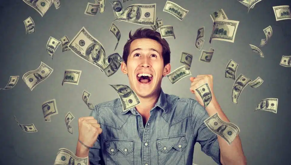 An extremely man watching money come falling down around himl.