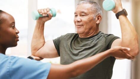 Medical, training and physiotherapy with dumbbell and old man with nurse for rehabilitation, support and retirement. Healthcare, help and physical therapy with patient and black woman in nursing home