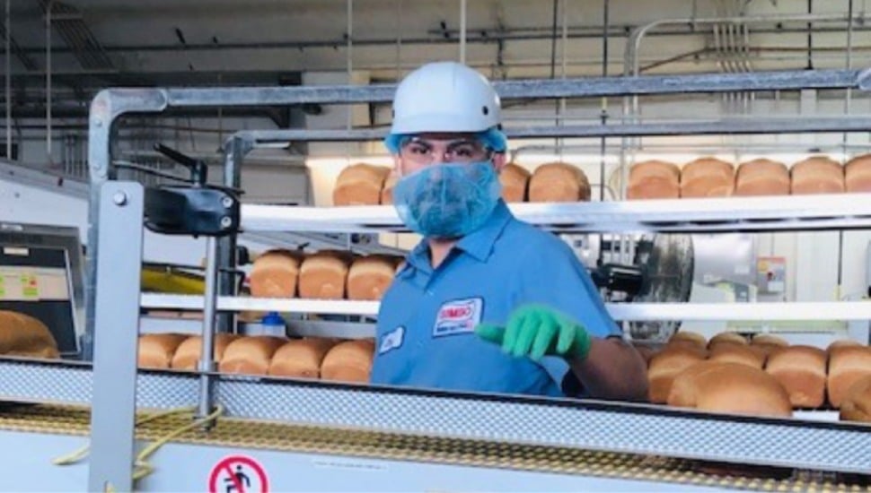 A masked factory worker at a factory assembly line for Bimbo Bakeries.