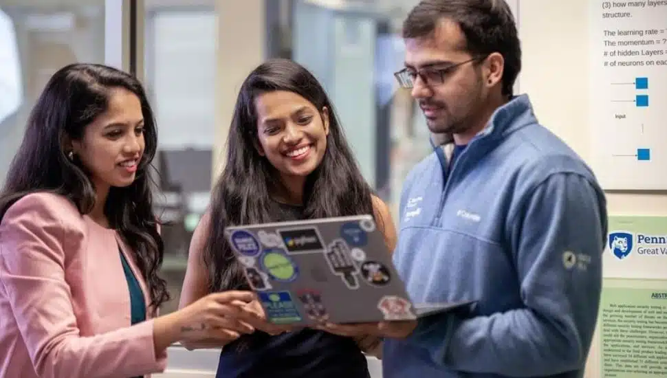 Three people standing around a laptop while one man holds it