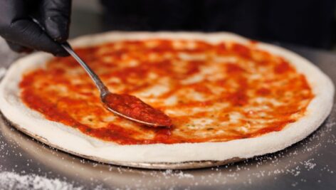 chef spreads tomato sauce on a pizza pan