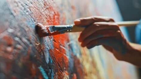 A hand takes a paint brush to a canvas, creating a colorful work of art.