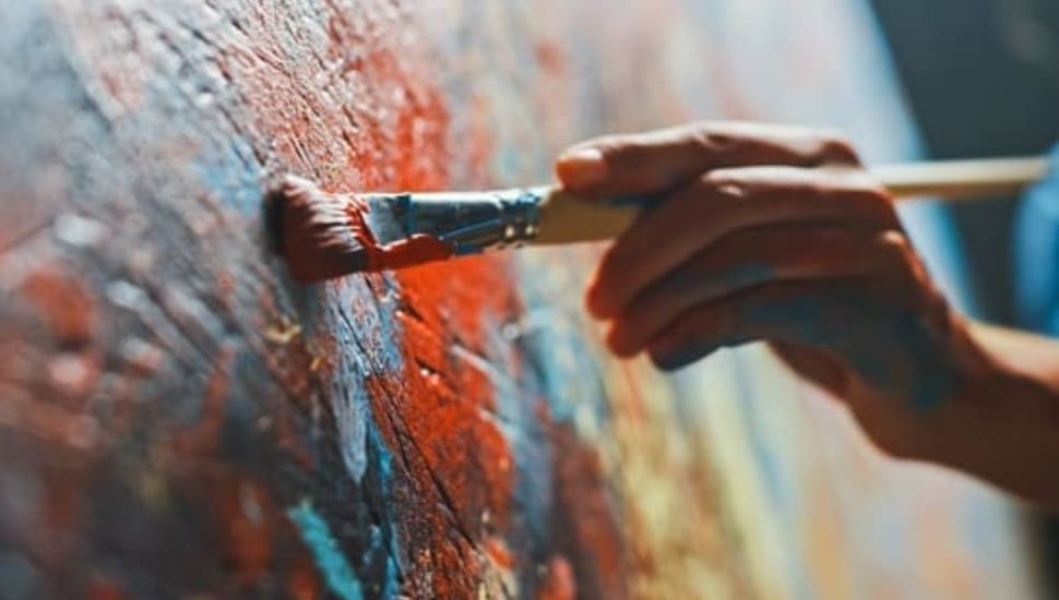 A hand takes a paint brush to a canvas, creating a colorful work of art.