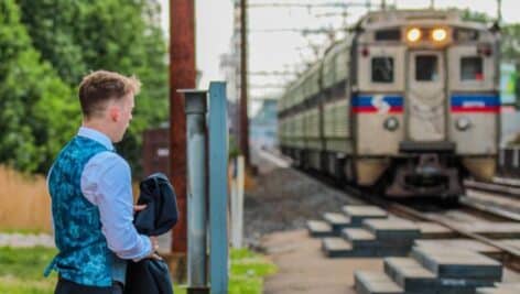 A man in formal attire waits at the regional rail train platform as a train pulls into the station.