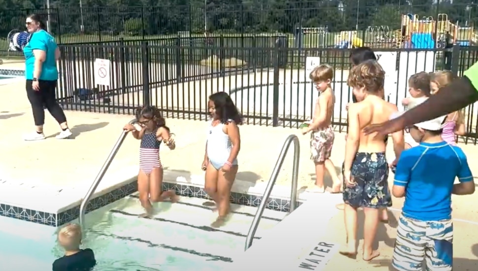 Children going into pool for lessons with adults supervising.