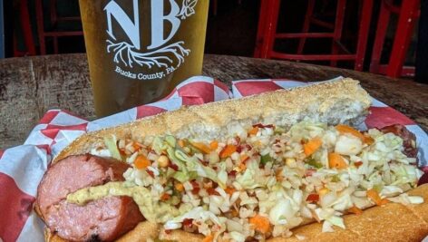 hot dog topped with mustard, cabbage, carrots in front of beer