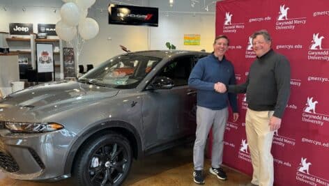 two men standing in front of gwynedd Mercy backdrop next to car