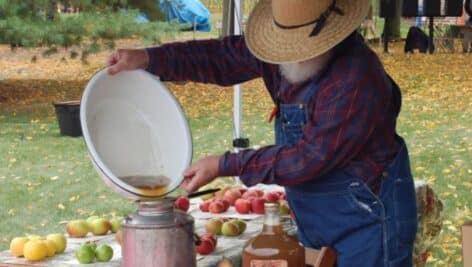 A farmer making apple cider with fresh apples at the Annual Apple Butter Frolic.