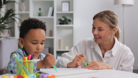 A woman therapist works with a young African American boy while he does some drawing.