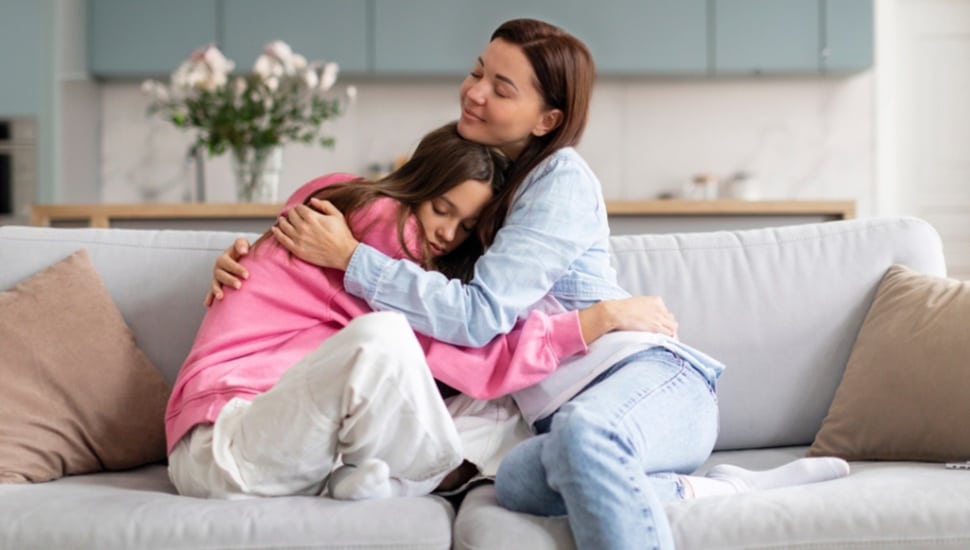 A woman comforts a teenage girl in her home.