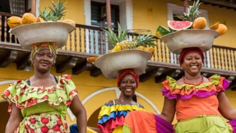 Three women holding baskets of fruit on their heads.