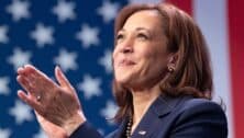 Kamala Harris applauds in front of an American flag backdrop.